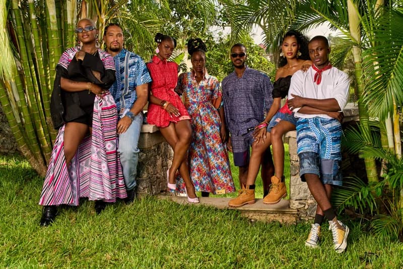A group of six models are posing in an outdoor setting showcasing a new clothing line. The models are wearing various garments that appear to be made of colorful patterned fabrics. The photo is well-lit and the models are styled in modern clothes.