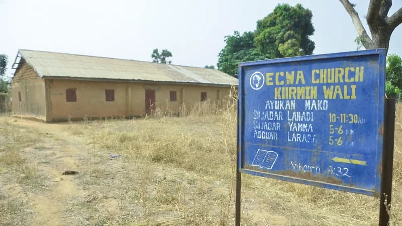 The image shows the ECWA Church Kurmin Wali, likely located in Nigeria. A blue sign provides the church's name and service times. The building itself appears to be a simple, rural structure.
