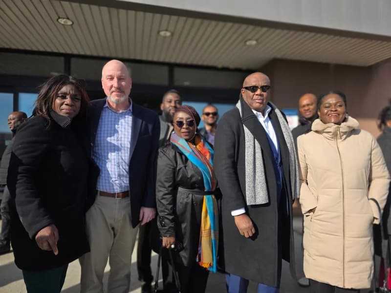 A Ghanaian delegation and officials pose for a group photograph outside a building during a visit to the Philadelphia Port. The individuals are dressed in business and winter attire, including heavy coats and scarves, indicating a formal diplomatic or business meeting in a cold climate.