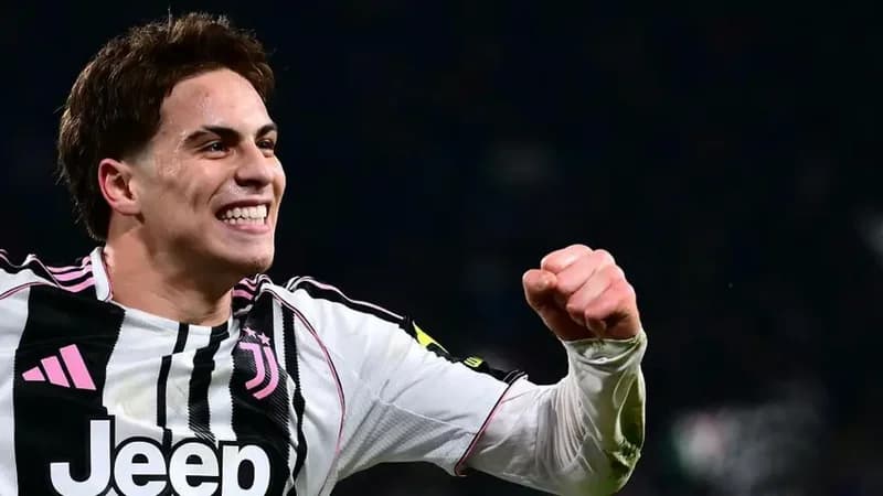 Juventus forward Kenan Yildiz celebrates with a clenched fist and a wide smile during a football match. He is wearing the official black and white striped Juventus home jersey featuring pink accents and the Jeep sponsor logo.