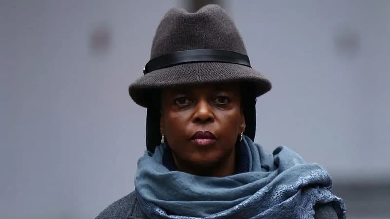 A close-up portrait of Diezani Alison-Madueke, Nigeria's former petroleum minister, looking directly at the camera with a serious expression. She is dressed in a grey fedora-style hat with a black band, a blue-grey scarf, and a grey coat against a neutral, blurred background.