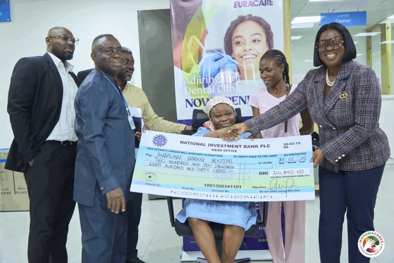 A group of individuals are seen presenting a large ceremonial check for GH‵210,840.00 to a woman seated in a wheelchair, who appears to be the medical patient mentioned in the news story. The woman on the right, dressed in a professional blazer, shakes hands with the patient while holding the check, which is issued from the National Investment Bank PLC to Euracare Spring Hospital.