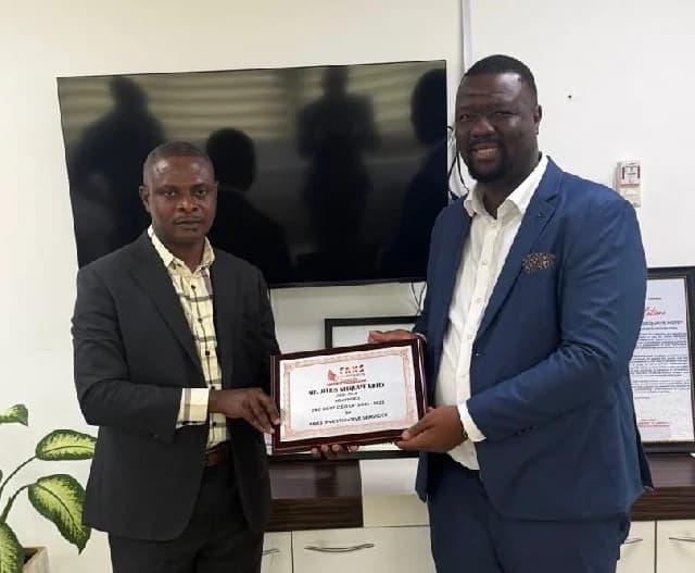 Mr. Julius Neequaye Kotey, CEO of PSCU, is pictured receiving a commemorative plaque from a representative of FAKS Investigative Services. The two men are standing in an office setting, holding the award which recognizes Kotey as the 2nd Best CEO for the year.
