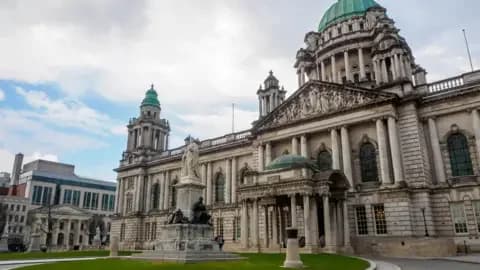 Getty Images A stock image showing the exterior of Belfast City Hall during the day. It is an ornate grey building with copper green tower domes.
