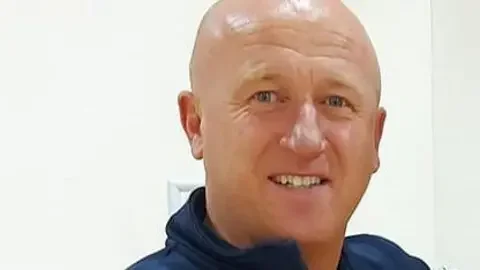 Kevin Lynch, who has a bald head and is clean shaven, smiles at the camera.