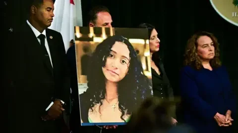 Getty Images A portrait of the late Celeste Rivas Hernandez is shown during a press briefing by the Los Angeles County District Attorney and is flanked by other officials.