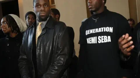 Gamma-Rapho via Getty Images Seba standing on the left and a man in a black T-shirt with the words generation Kemi Seba written on it, on the right.