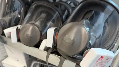 Two grey masks are displayed in a rack with clear panels for the face.