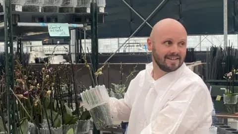 Stefan Kuiper wears a protective white suit and looks out of shot. Behind him are shelves of orchid plants.
