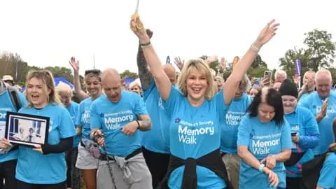 Getty Images A woman, Ruth Langsford, stood at the front of a group of people while waving her hands in the air. All of the people in the walk are wearing blue t-shirts.