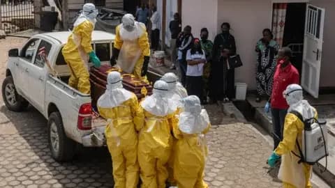 EPA Health workers wearing full personal protective equipment (PPE) lift a coffin of a victim on to the back of a pick-up truck in Bunia. Some people with masks watch them outside a hospital.