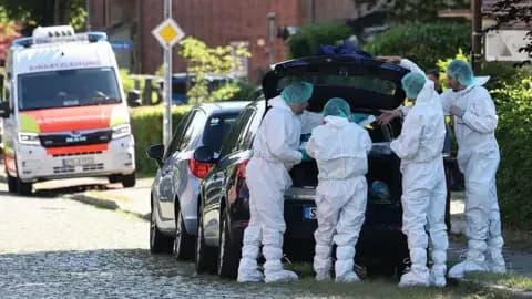 AFP via Getty Images A group of officials in forensic uniforms gathered around the open boot of a black car on the side of a road in Germany.