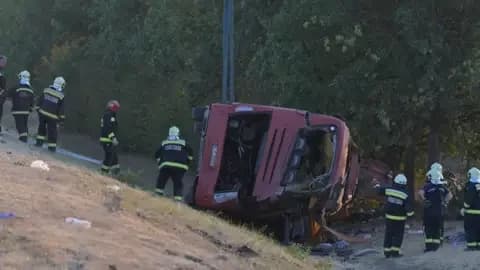 EPA A crumpled red bus sits at the bottom of a ravine as firefighters attend.