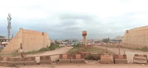 Concrete bridge structures on an interchange stand partially uncompleted at the old Kpone Barrier while traffic is diverted onto temporary routes, causing congestion and delays for motorists