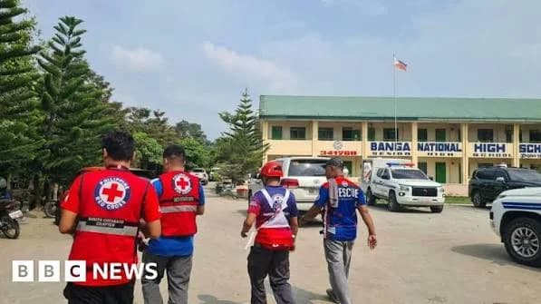 Philippine Red Cross and rescue personnel arrive at Banga National High School following a reported shooting incident. Emergency vehicles are parked in the school's courtyard in front of the main building where the Philippine national flag is visible.