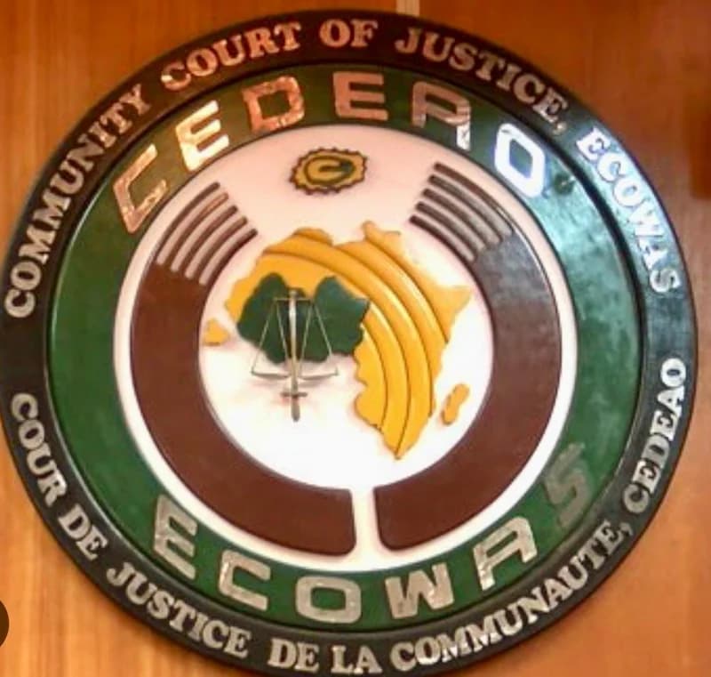 The image features a close-up of the official circular seal of the ECOWAS Community Court of Justice mounted on a wooden wall. The seal displays a map of Africa with a scales of justice symbol at the center, surrounded by the organization's name in both English and French.