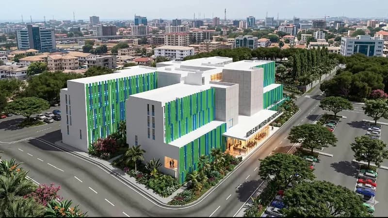 An architectural rendering of the proposed Korle-Bu Mother and Child Centre, showing a modern white multi-story building with distinctive green and blue facade details. The structure is depicted within a landscaped urban environment featuring organized parking lots and a city skyline in the background.