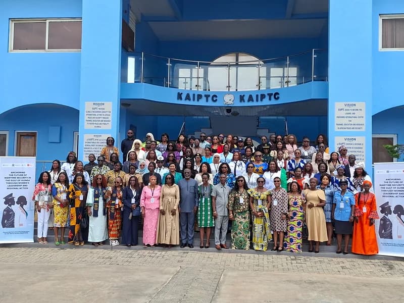 A large group of participants, predominantly women in formal and military attire, pose for a group photograph in front of the Kofi Annan International Peacekeeping Training Centre (KAIPTC) in Accra. The attendees are gathered for a regional summit focused on strengthening maritime security in the Gulf of Guinea through women's leadership.