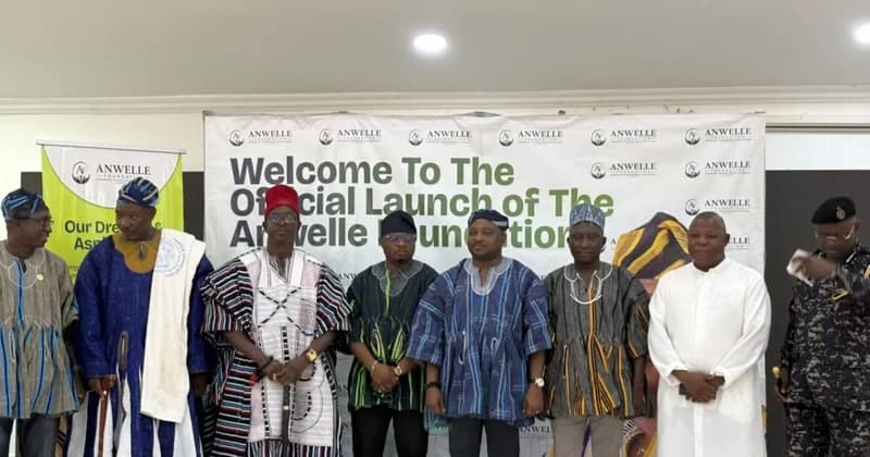 A group of men, including local dignitaries and a police officer, pose in front of a banner for the official launch of the Anwelle Foundation. Many of the men are wearing traditional Ghanaian northern smocks (fugu), reflecting the cultural context of the event held in Jirapa.