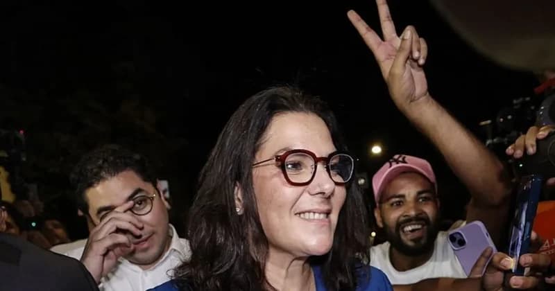 A photograph shows a smiling woman wearing red-framed glasses, identified as a prominent Moroccan politician, surrounded by supporters during a nighttime celebration. To her right, a hand is raised in a victory sign while another person captures the scene on a smartphone.
