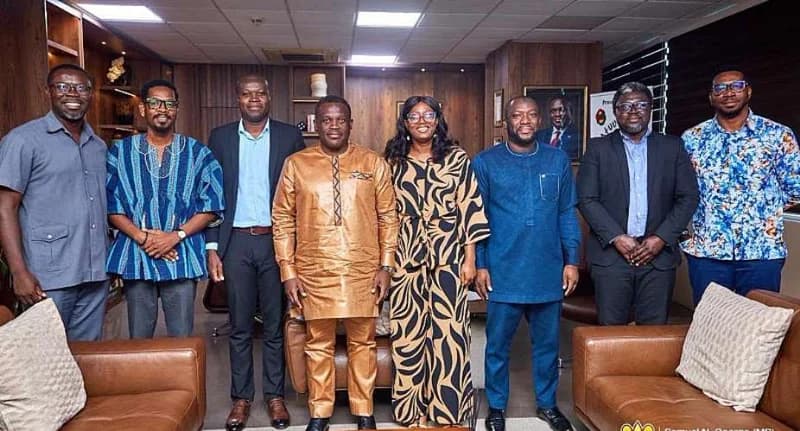 A group of eight professionals, including Ghanaian Member of Parliament Sam George, stand for a commemorative photograph in a formal office setting. The group is dressed in a mix of corporate suits and traditional Ghanaian attire, suggesting a high-level government or sector-specific meeting.