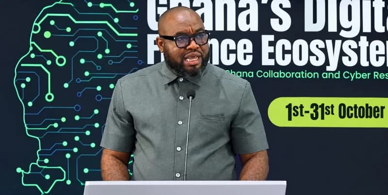 Dr. Albert Antwi-Boasiako, Director-General of Ghana's Cyber Security Authority, is seen speaking at a podium during a cybersecurity-focused event. The backdrop features digital circuitry graphics and text highlighting Ghana's Digital Finance Ecosystem and Cyber Resilience Month.