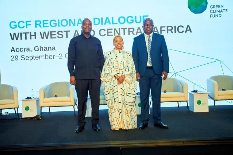 Three officials stand on a stage during the GCF Regional Dialogue with West and Central Africa in Accra, Ghana. The background features a large banner with the event title and the Green Climate Fund logo, alongside seating for a panel discussion.