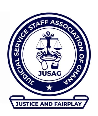 The image displays the official logo of the Judicial Service Staff Association of Ghana (JUSAG). It features a circular emblem with the scales of justice held by two hands, symbolizing the association's role in the judicial system. The colors are navy blue and white, with the motto 'Justice and Fairplay' at the bottom.