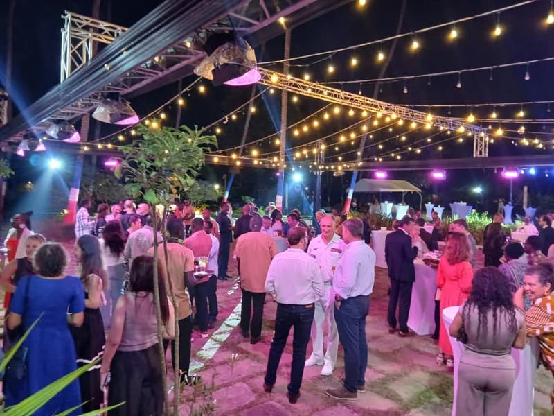 A vibrant outdoor networking event held at night, featuring members of the French and Ghanaian business communities. Guests are seen socializing under a canopy of warm string lights and professional stage lighting, creating a collaborative atmosphere for economic discussion.