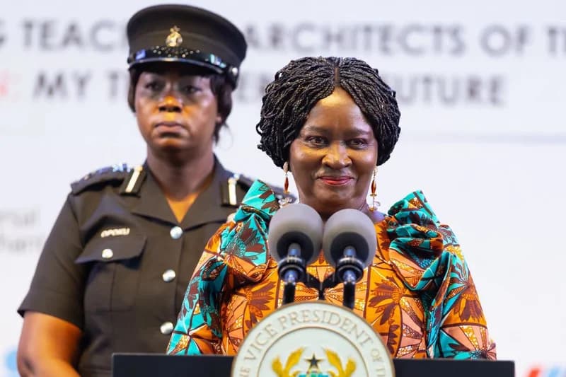 Vice President Professor Naana Jane Opoku-Agyemang is pictured delivering a speech at a formal event. She stands behind a podium bearing the Seal of the Vice President, accompanied by a female security officer in a police uniform against a backdrop referencing teachers.