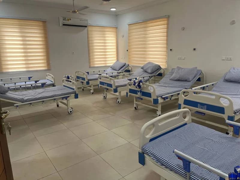 A photograph of a clean, well-lit hospital ward containing several modern hospital beds with blue and white striped linens. Decorative ribbons on some of the bed frames suggest a recent commissioning or inauguration ceremony for a health facility.