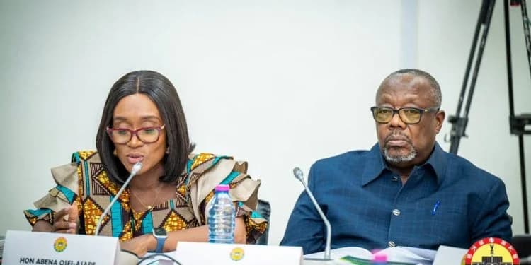 Hon. Abena Osei-Asare is captured speaking during a formal parliamentary proceeding, likely a session of the Public Accounts Committee (PAC) in Ghana. She is seated next to a male official, with both individuals positioned behind microphones and nameplates on a panel.