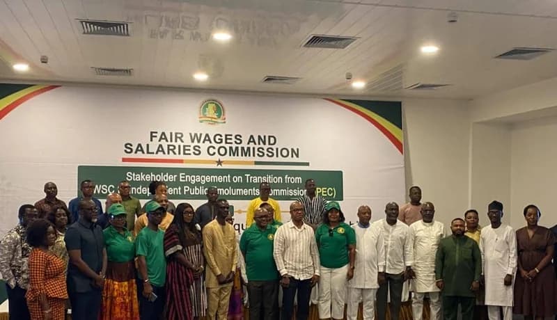 A group of approximately 28 stakeholders and officials posing for a group photograph during a formal event. They are standing in front of a large white backdrop featuring the logo and name of the Fair Wages and Salaries Commission (FWSC).