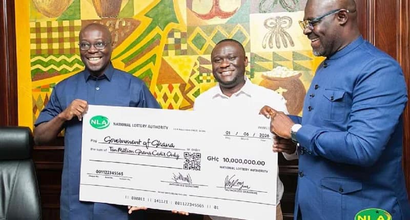 Three officials are pictured smiling during a formal ceremony where the National Lottery Authority (NLA) presented a GH¢10 million dividend check to the Government of Ghana. The presentation features a large symbolic check held against a backdrop of traditional Ghanaian artwork and Adinkra symbols.
