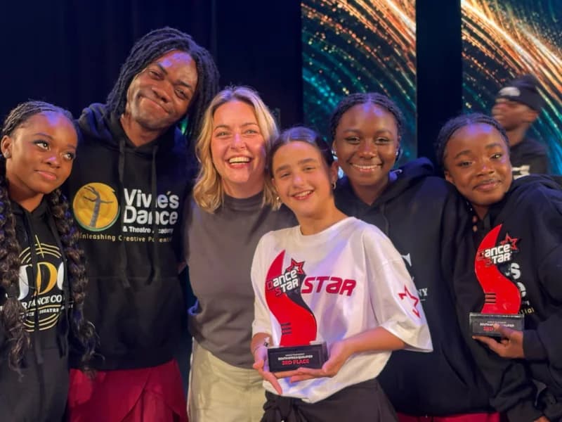 A group of dancers and staff from Ghana's Vivie’s Dance and Theatre Academy celebrate their success at a competition. They are seen smiling while holding red 'DanceStar' trophies, with one clearly marked for a 3rd place finish at a South Africa qualifier event.