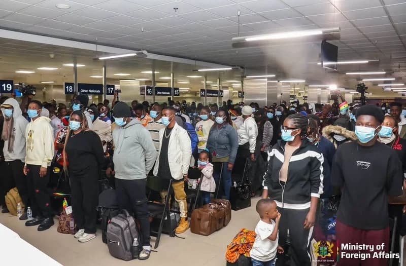 A large group of people, many wearing face masks and carrying backpacks and luggage, stand in an immigration processing area. The scene features numbered counters and signage for 'Other Nationals' and 'ECOWAS Nationals', with a watermark from the Ghanaian Ministry of Foreign Affairs visible in the corner.