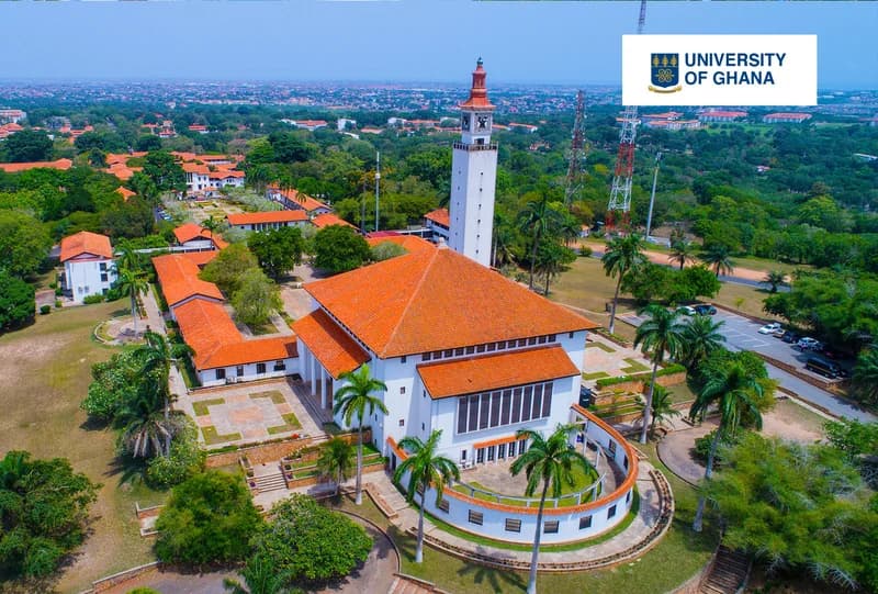 An aerial photograph of the University of Ghana, Legon campus, featuring the distinctive white buildings with orange-tiled roofs and the iconic Balme Library clock tower. The sprawling campus is surrounded by lush green trees and landscape, representing one of the major public universities in Ghana.