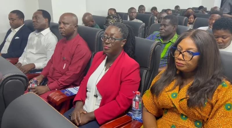 A group of professionals and stakeholders are seated in an auditorium during a formal engagement session. The participants, dressed in a mix of Western business attire and traditional Ghanaian fabrics, appear focused on a presentation or speaker off-camera.