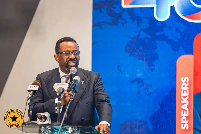 A man in a dark suit and glasses delivers a speech at a podium equipped with several microphones. The official logo of the Bank of Ghana is visible in the lower left corner, while the word SPEAKERS appears on a red graphic in the background.