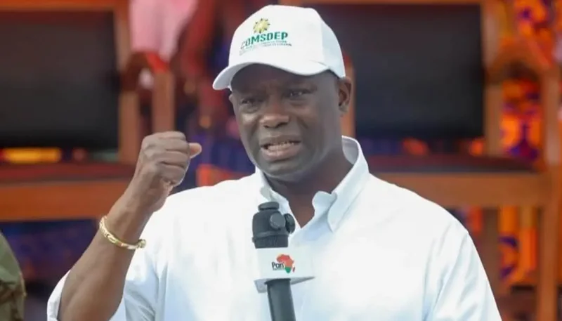 A close-up photograph of a Ghanaian official, likely the Minister for Lands and Natural Resources, speaking passionately into a microphone. He is wearing a white branded cap and a white shirt, gesturing with a clenched fist to emphasize his point during an official event.
