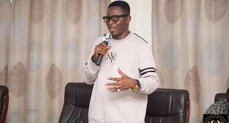 Rashid Tanko Computer, the Administrator (CEO) of the Ghana Investment Fund for Electronic Communications (GIFEC), is captured speaking into a microphone. He is dressed in a light grey sweatshirt featuring the 'NYC' logo and is gesturing with his left hand while addressing an audience indoors.