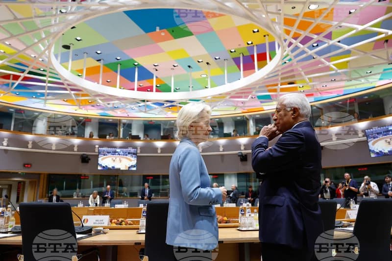 European Commission President Ursula von der Leyen and former Portuguese Prime Minister António Costa engage in a private conversation during a diplomatic summit. They are standing in a large conference hall notable for its vibrant, multicolored checkered ceiling and circular lighting fixture.