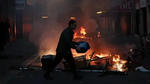 Reuters A man tries to extinguish a fire, during civil unrest, the day after a national day of demonstrations against the cost of living and rising fuel prices, in Paris, France, October 18, 2026.