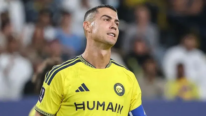 Cristiano Ronaldo is captured in a close-up shot during a football match, looking upwards with a frustrated or disappointed expression. He is wearing his yellow Al Nassr FC jersey with a captain's armband against a blurred background of stadium spectators.
