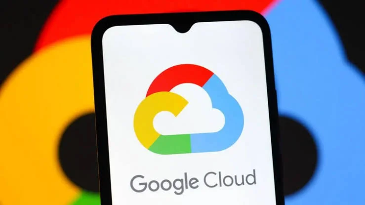 A photograph showing a smartphone screen displaying the colorful Google Cloud logo and text. The background features a blurred, larger version of the standard Google logo, emphasizing the corporate brand. This image represents the service provider involved in the recent cloud infrastructure resolution.