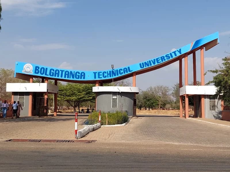 The image shows the main entrance gate of Bolgatanga Technical University under a clear blue sky. A prominent curved blue sign with the university's name spans across red pillars, with security booths and pedestrians visible at the entrance.
